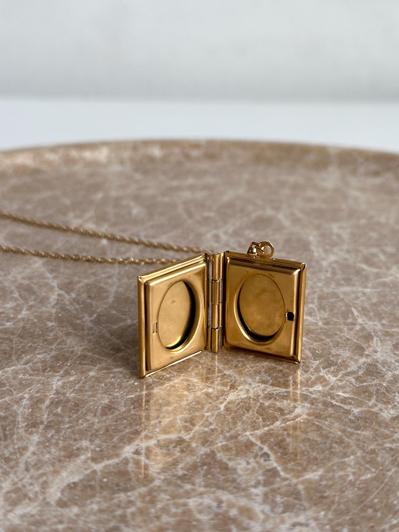 May include: A gold-toned locket necklace with a book-shaped pendant. The locket opens to reveal two oval-shaped compartments.