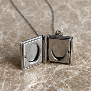 May include: A silver chain necklace with a silver locket pendant. The locket is open and has two oval-shaped photo slots.