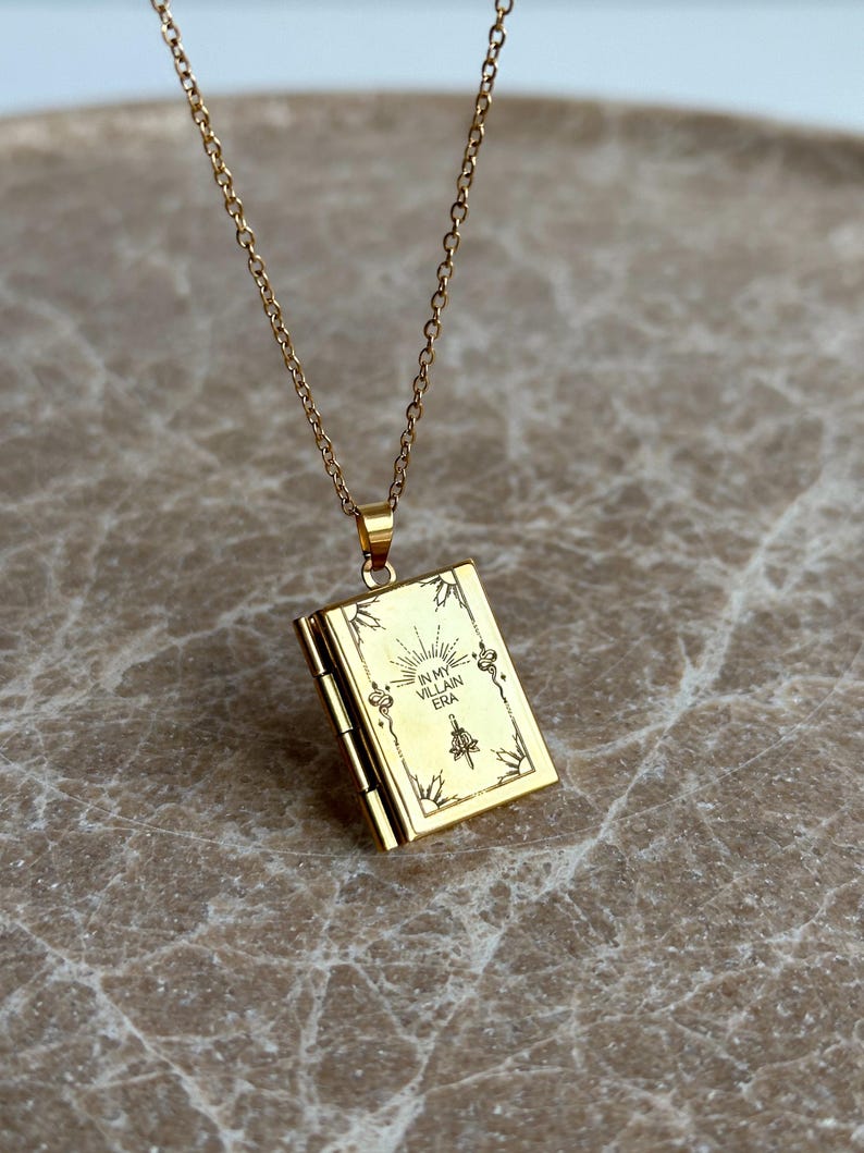 May include: Gold chain necklace with a gold locket pendant. The locket is engraved with the words "In My Villain Era".