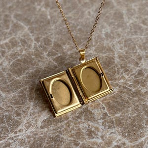 May include: Gold-toned necklace with a locket pendant shaped like an open book. The locket has two oval-shaped photo slots.