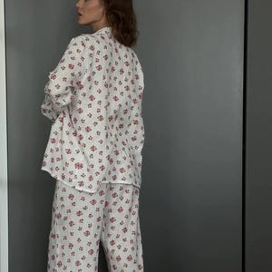 May include: White pajama set with a floral pattern in shades of red. The set includes a long-sleeved button-down shirt and matching wide-leg pants. The fabric appears to be lightweight and comfortable, suitable for sleepwear.