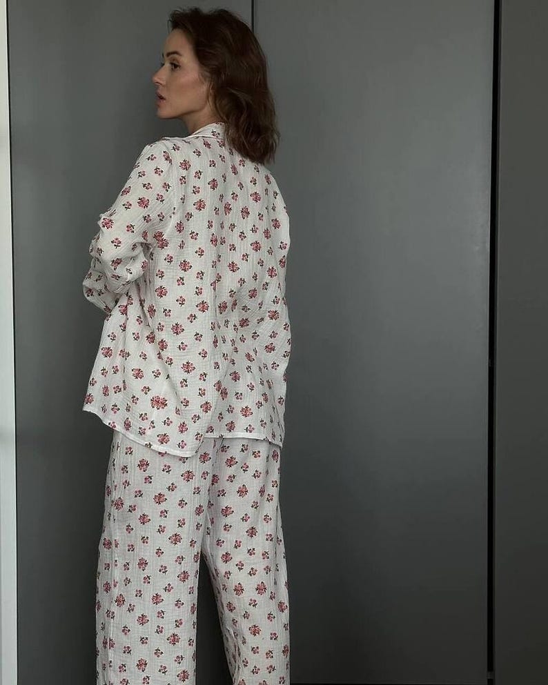 May include: White pajama set with a floral pattern in shades of red. The set includes a long-sleeved button-down shirt and matching wide-leg pants. The fabric appears to be lightweight and comfortable, suitable for sleepwear.