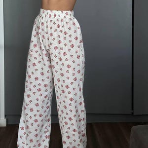 May include: White wide-leg pants with a repeating pattern of small pink flowers. The pants have a high waist and a loose, flowing fit, made of a lightweight fabric. The floral print adds a touch of femininity to the casual design.