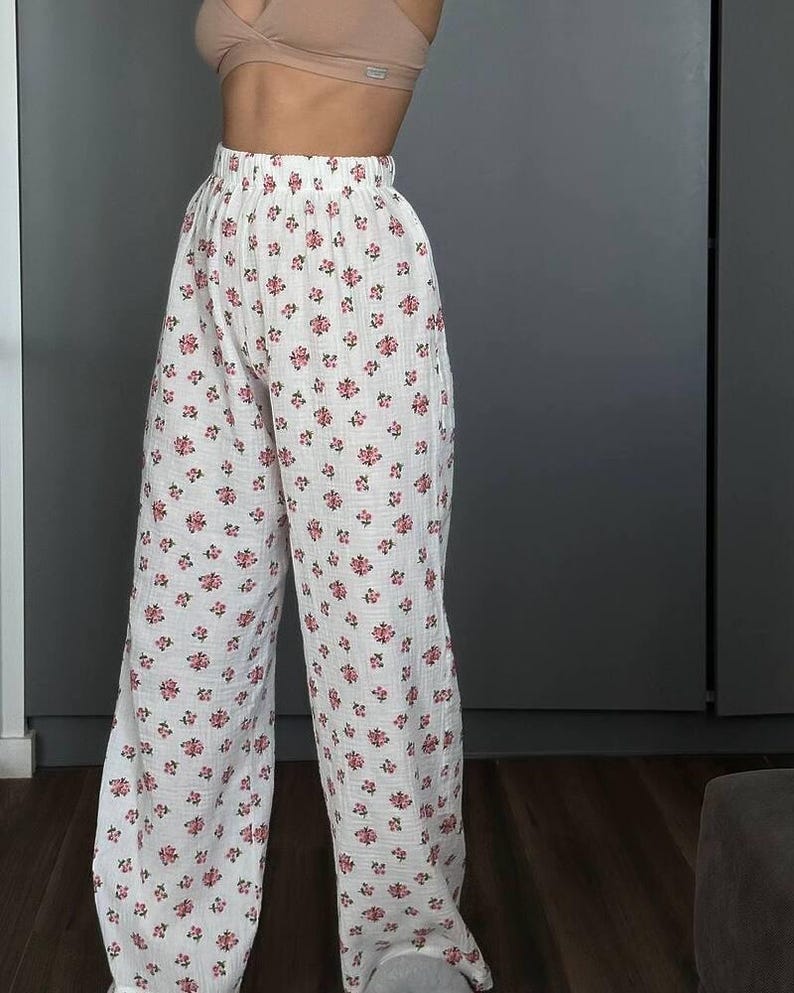 May include: White wide-leg pants with a repeating pattern of small pink flowers. The pants have a high waist and a loose, flowing fit, made of a lightweight fabric. The floral print adds a touch of femininity to the casual design.
