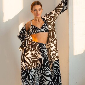 Puede incluir: Un conjunto a juego con estampado en blanco y negro que consta de un top de sujetador, pantalones de cintura alta y una chaqueta de manga larga. El conjunto tiene un dise&ntilde;o abstracto y audaz. La modelo lleva un delicado collar.