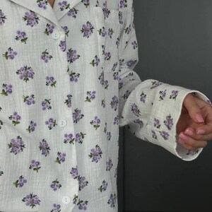 May include: White pajama set with a delicate floral pattern in shades of purple and green. The long-sleeved top features a button-down front and a chest pocket. The fabric appears soft and lightweight, ideal for sleepwear.