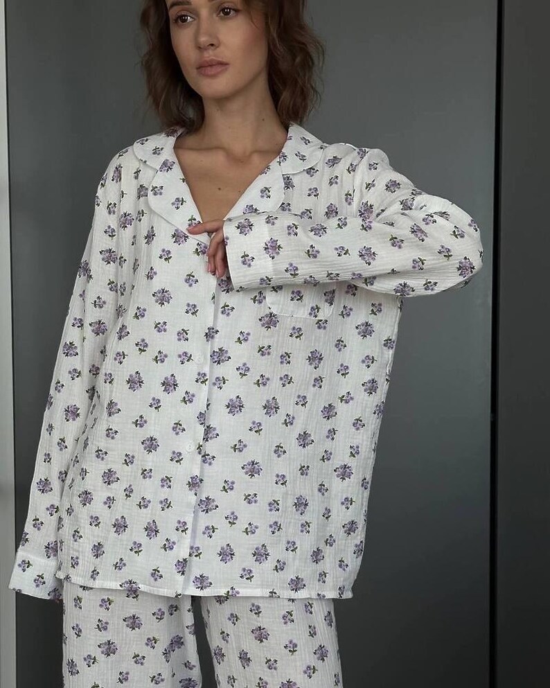 May include: White pajama set with a delicate floral pattern in shades of purple. The set includes a button-down shirt with a collar and a pair of matching pants. The fabric appears soft and lightweight, perfect for comfortable sleepwear.