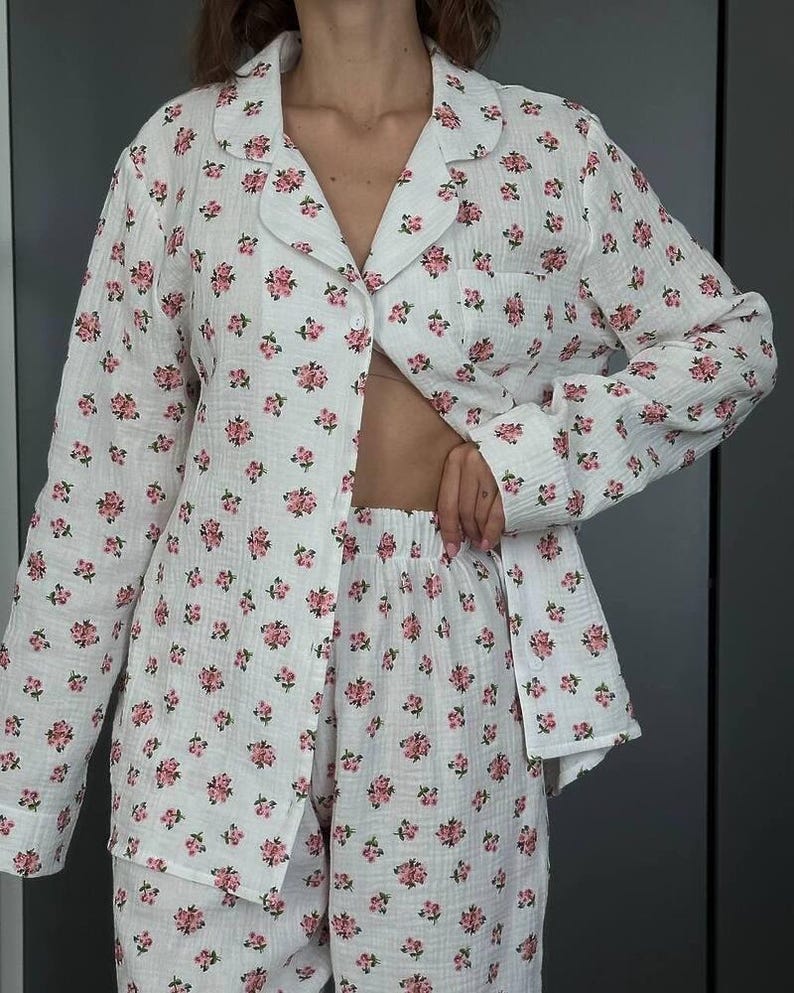May include: White pajama set with a pink floral pattern. The set includes a button-down shirt with a chest pocket and matching shorts. The fabric appears to be a lightweight, textured material.