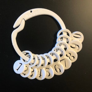 May include: White plastic ring with a clip and numbered rings. The numbers on the rings are 1 through 10.