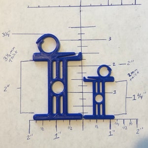 May include: Two blue plastic objects, resembling stylized figures, are displayed against a grid background. The larger object is approximately 3.75 inches tall and 1 inch wide. The smaller object is about 2 inches tall and 1 inch wide. Measurements are in inches.