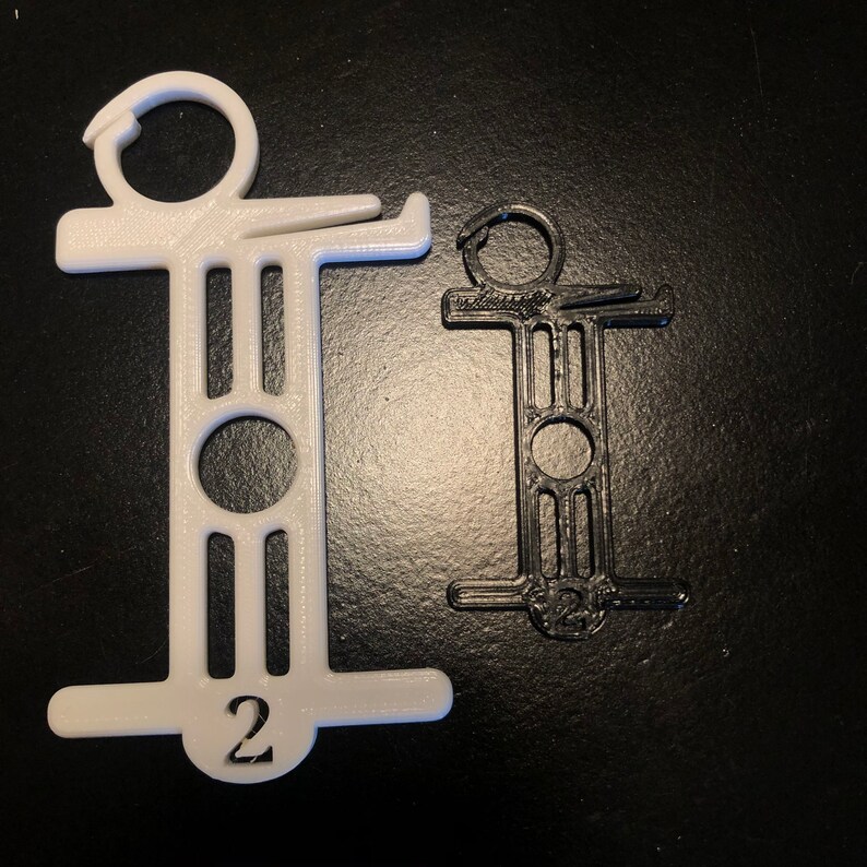 May include: Two plastic, 3D-printed hanger organizers. One is white, the other black. Both have a hook at the top, a circular opening, and the number "2" at the bottom. The design is a stylized "T" shape.