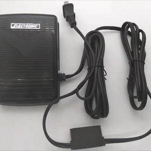 May include: Black electronic sewing machine foot pedal with a power cord. The pedal has the word "ELECTRONIC" printed on it. The power cord is black and has a two-prong plug.