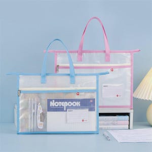 May include: Two clear mesh tote bags with blue and pink accents. The bags have zippered closures and handles. One bag has blue trim and handles, the other has pink. The front bag contains a notebook and stationery.