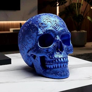 Könnte beinhalten: Eine leuchtend blaue Totenkopfskulptur mit komplizierten, geprägten Blumen- und geometrischen Schnörkelmustern auf der gesamten Oberfläche. Das Objekt zeigt eine detaillierte anatomische Struktur mit hohlen Augenhöhlen, Nasenhöhle und Zähnen.