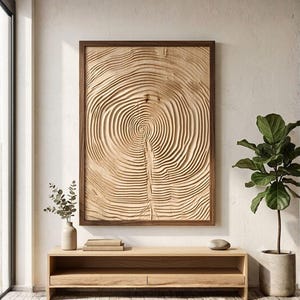 May include: A rectangular wall art piece featuring a light-colored wood panel with deep, concentric circular carvings that mimic the appearance of tree rings. The artwork is encased in a dark brown wooden frame and mounted on a plain wall.