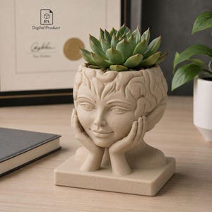 Puede incluir: Una maceta beige con forma de cabeza humana con las manos bajo la barbilla, que presenta una textura similar a un cerebro en la parte superior. Una suculenta verde está plantada en el interior. La maceta se asienta sobre una base cuadrada.