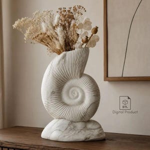 Könnte beinhalten: Eine weiß marmorierte Vase in Form eines spiralförmigen Ammoniten-Gehäuses auf einem festen Sockel. Die Vase enthält ein Trockenblumenarrangement mit beigen und cremefarbenen Gräsern und Samenkapseln. Ein kleines Symbol mit dem Text STL Digital Product.