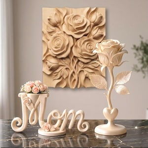 Può includere: Un insieme di oggetti decorativi color crema, tra cui un'arte murale di rose in legno intagliato, una scultura a forma di rosa e una composizione floreale con la scritta 'Mamma'. Gli oggetti sono su una superficie scura, simile al marmo.