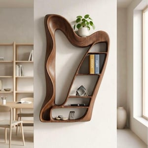 Può includere: Una mensola a muro a forma di arpa in legno scuro. Presenta diversi scomparti che contengono una piccola pianta in vaso, libri, un cristallo, una penna e pietre decorative. La mensola è fissata a una parete bianca.