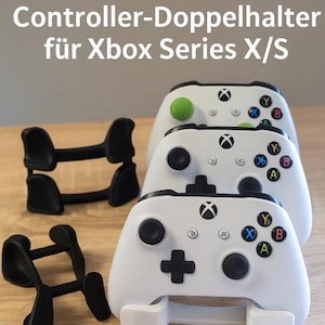 Könnte beinhalten: Ein weißer Xbox Series X/S Controller-Ständer mit drei weißen Controllern darauf. Der Ständer ist aus Kunststoff und hat eine schwarze Basis. Die Controller sind alle nach vorne gerichtet und haben das Xbox-Logo auf der Vorderseite. Der Ständer ist so konzipiert, dass er zwei Controller aufrecht und einen Controller horizontal hält.