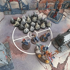 Könnte beinhalten: Ein Tabletop-Spielset mit einer Vielzahl von Miniaturfiguren, darunter eine große, detaillierte Figur in der Mitte. Die Figuren sind in Grautönen und Weiß bemalt und auf einer runden Basis angeordnet. Das Spielbrett besteht aus einem dunklen, strukturierten Material und verfügt über eine Vielzahl von Gebäuden und anderen Strukturen.