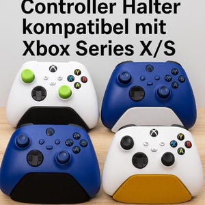 Könnte beinhalten: Vier Xbox Series X/S Controller in verschiedenen Farben, weiß, blau und schwarz, werden auf einer Holzoberfläche angezeigt. Die Controller sind auf einem Ständer montiert, der sie aufrecht hält. Der Ständer ist weiß und hat eine gelbe Basis.