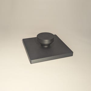 May include: A black square-shaped stamp with a round black knob on top.