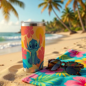 May include: A stainless steel tumbler featuring a cartoon character design with a tropical floral pattern. The tumbler is on a sandy beach with sunglasses and a colorful towel. Palm trees and ocean in the background.