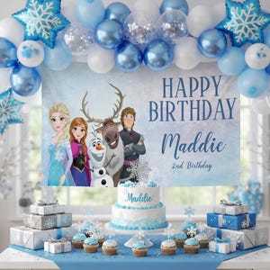 May include: A festive birthday party scene with a blue and white theme. A banner reads "Happy Birthday Maddie" with the characters from the movie Frozen. A cake, cupcakes, and wrapped gifts are on a table decorated with balloons and snowflake accents.