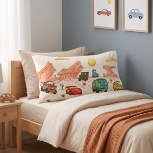 May include: A rectangular pillowcase featuring a desert landscape illustration with various cartoon vehicles, including a red race car, a brown tow truck, a green van, and a yellow car, set against a cream background with orange rock formations.