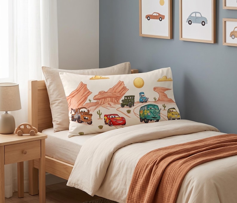 May include: A rectangular pillowcase featuring a desert landscape illustration with various cartoon vehicles, including a red race car, a brown tow truck, a green van, and a yellow car, set against a cream background with orange rock formations.