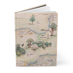 Könnte beinhalten: Ein Hardcover-Journal mit einem skurrilen Kartendesign. Die Karte zeigt Illustrationen von Bäumen, Häusern und einem Fluss, mit Textbeschriftungen wie "My House" und "100 Aker Wood". Das Journal ist geöffnet und zeigt leere Seiten.