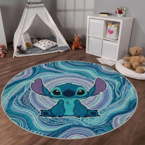 Può includere: Un tappeto circolare caratterizzato da uno sfondo in stile puntinista blu e viola con motivi vorticosi. Al centro del tappeto si trova un'illustrazione grafica di un personaggio alieno blu con grandi orecchie, occhi scuri e un naso piccolo, realizzato in stile puntinato.