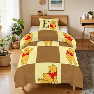 May include: A Winnie the Pooh themed bedding set featuring a comforter, pillow, and bedspread. The comforter and bedspread have a brown and yellow checkered pattern with images of Winnie the Pooh. The pillow has the letter "E" and the name "EDWARD".
