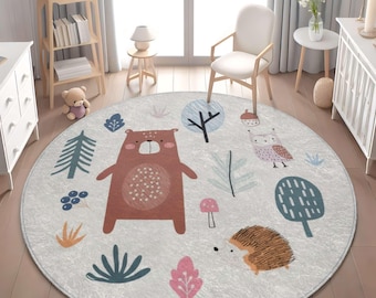 May include: A round area rug featuring a light gray background with a repeating pattern of a brown bear, a hedgehog, and an owl. The design includes stylized trees, mushrooms, and leaves in muted shades of blue, pink, and orange across the surface.