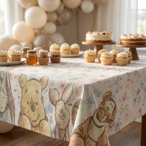 May include: A rectangular tablecloth featuring a watercolor-style print of Winnie the Pooh, Piglet, and Tigger surrounded by small pink and blue flowers. The fabric is draped over a table set with cupcakes, honey jars, and two round cakes.