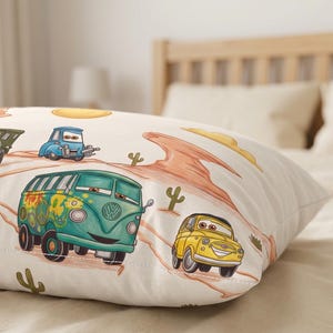 May include: A rectangular pillowcase featuring a cream-colored background with a desert landscape print. The design includes cartoon-style vehicles, including a teal van with flower decals, a yellow car, and a green truck, alongside orange rock formations and cacti.