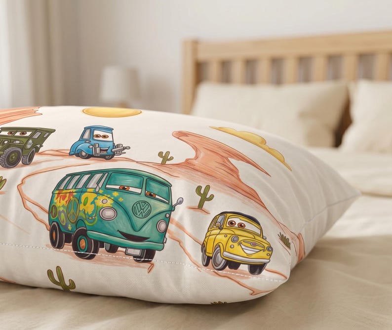 May include: A rectangular pillowcase featuring a cream-colored background with a desert landscape print. The design includes cartoon-style vehicles, including a teal van with flower decals, a yellow car, and a green truck, alongside orange rock formations and cacti.