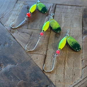 May include: Three fishing lures with yellow and green bodies and red beads. The lures have a silver hook and are designed for catching fish.