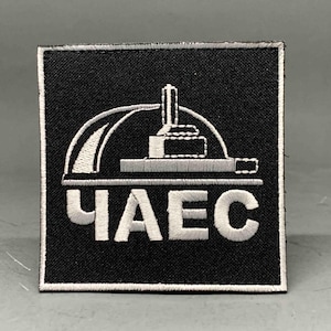 Pode incluir: Patch quadrado preto com design bordado branco e texto cirílico. O design apresenta uma estrutura estilizada com um arco curvo e uma torre. O texto "ЧАЕС" é bordado em branco.