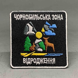 Pode incluir: Patch quadrado preto com borda branca com texto e imagens bordadas. O texto diz "ЧОРНОБИЛЬСЬКА ЗОНА" e "ВІДРОДЖЕННЯ". O patch retrata uma paisagem com um veado, árvores e montanhas.