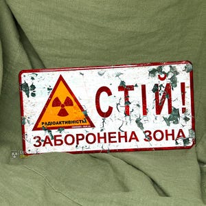 Könnte beinhalten: Rechteckiges Metallschild mit abgenutztem Finish, gelbem Dreieck mit Strahlungssymbol und den Worten "РАДІОАКТИВНОСТІ" und "ЗАБОРОНЕНА ЗОНА". Das Schild hat rote Schrift und einen weißen Hintergrund.