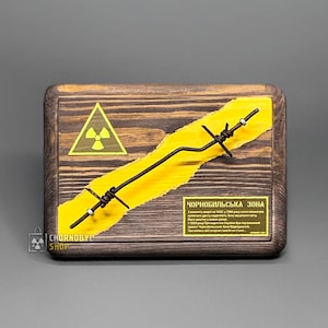 May include: Wooden plaque featuring a yellow radiation symbol and barbed wire. A yellow stripe runs across the plaque, with text reading "CHORNOBYL SHOP". The background is a dark grey.