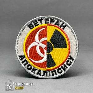 Può includere: Toppa ricamata circolare con design diviso. Una metà è rossa con un simbolo di pericolo biologico bianco, l'altra nera e gialla con un simbolo di radiazione. Le parole "VETERAN" e "APOKALIPSIS" sono ricamate sul bordo.