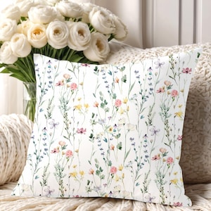 May include: White throw pillow with a floral pattern featuring watercolor-style pink, yellow, and blue wildflowers on green stems.