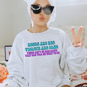 May include: A gray sweatshirt with the text "Roses are red, Violets are blue, There ain't no man alive that can tell me what to do" printed in blue and purple.