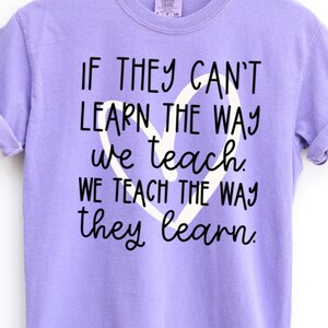 May include: A lilac Comfort Colors t-shirt with the text "IF THEY CAN'T LEARN THE WAY we teach WE TEACH THE WAY they learn" in black script. A white heart shape is behind the text. The shirt has short sleeves.