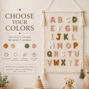 Peut inclure: Une tenture murale beige avec l'alphabet en différentes couleurs. Le texte "CHOOSE YOUR COLORS" est en haut, avec la possibilité de choisir 5 couleurs. La tenture a des glands et est faite de matériaux naturels.