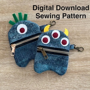 May include: Digital download sewing pattern for two denim monster coin purses. One monster has green spiky hair and one monster has three eyes and yellow horns. Both purses have a zipper closure and a gold zipper pull.