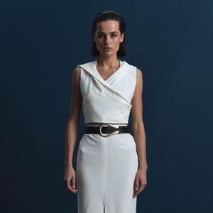 May include: A sleeveless white top and matching skirt with a high waist, paired with a black belt featuring a gold-colored buckle. The outfit is set against a dark blue background, creating a contrast.